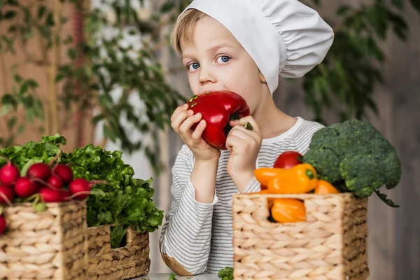 Niño guapo en uniforme de chef con verduras. Cocinar en la cocina en casa. Vegetariano. Alimento saludable — Foto de Stock
