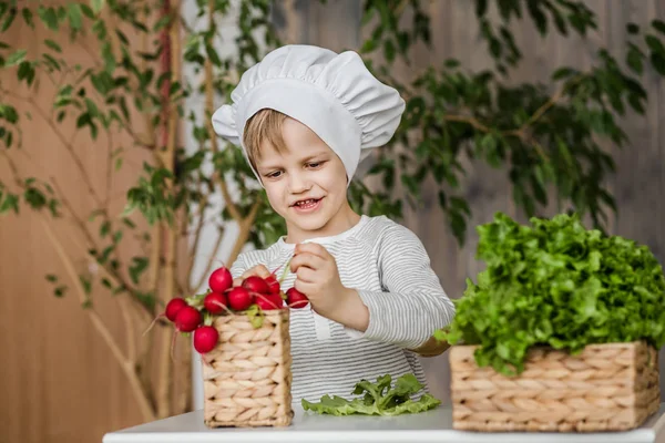 Un bel bambino in uniforme da chef con le verdure. Cucinare in cucina a casa. Vegetariano. Cibo sano — Foto Stock