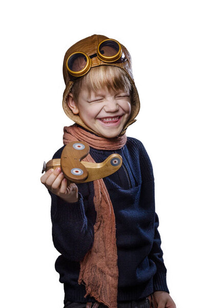 Счастливый ребенок в пилотской шляпе и очках. Ребёнок играет с деревянным игрушечным самолётом. Концепция мечты и свободы. Ретро. Студийный портрет на белом фоне
