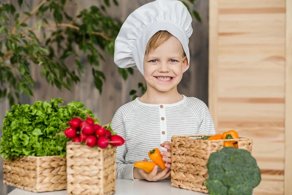 Garoto bonito em uniforme de chef com legumes. Cozinhar na cozinha em casa. Vegetariano. Alimentos saudáveis — Fotografia de Stock