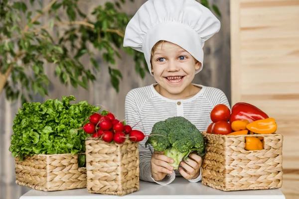 Lindo chico en uniforme de chef con verduras. Cocinar en la cocina en casa. Vegetariano. Alimento saludable — Foto de Stock