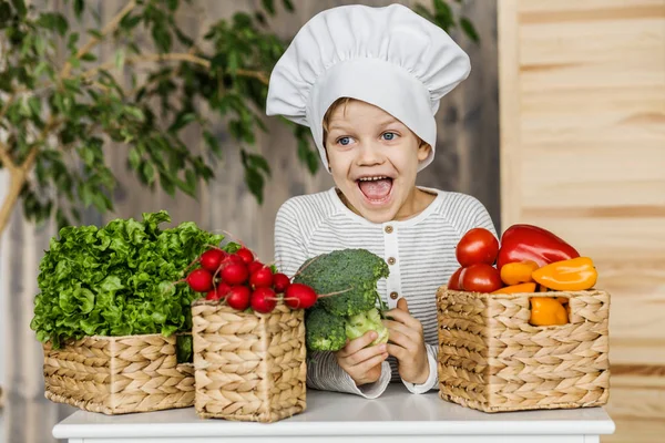 Lindo chico en uniforme de chef con verduras. Cocinar en la cocina en casa. Vegetariano. Alimento saludable — Foto de Stock