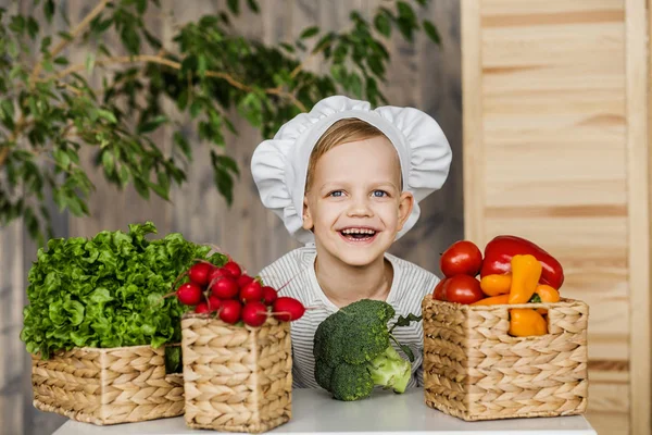 Niño guapo en uniforme de chef con verduras. Cocinar en la cocina en casa. Vegetariano. Alimento saludable —  Fotos de Stock