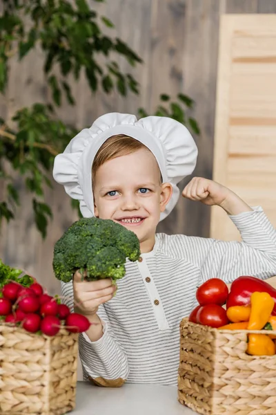 Niño guapo en uniforme de chef con verduras. Cocinar en la cocina en casa. Vegetariano. Alimento saludable — Foto de Stock