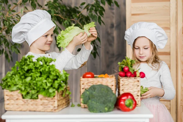 Handsome boy and beautiful young girl playing in the kitchen chefs. Healthy food — Stock Photo, Image