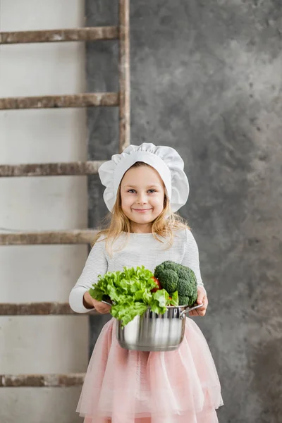 Piccola bella ragazza che tiene una pentola piena di verdure. Cibo sano. Vendemmia. Piccola casalinga — Foto Stock