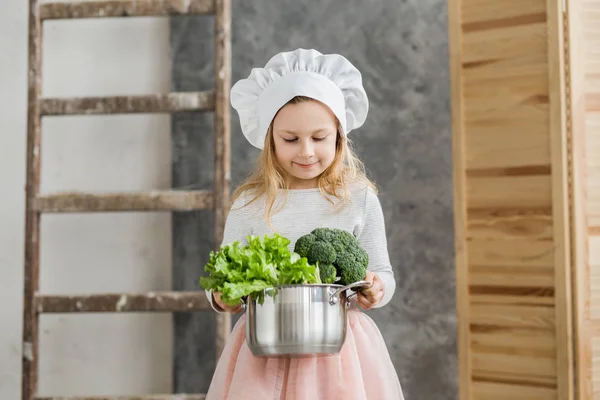 Piccola bella ragazza che tiene una pentola piena di verdure. Cibo sano. Vendemmia. Piccola casalinga — Foto Stock