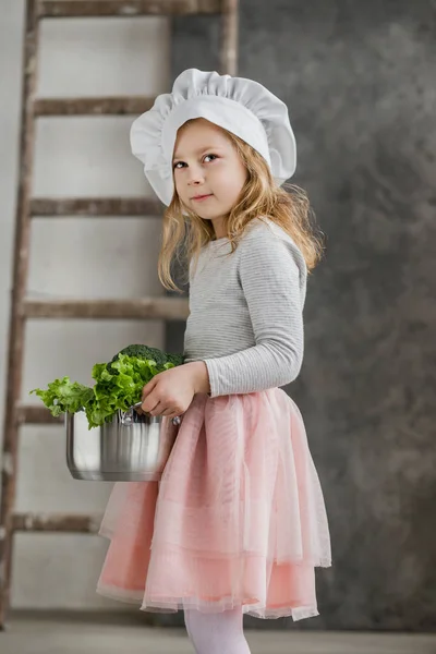 Niña hermosa sosteniendo una olla llena de verduras. Comida saludable. Cosecha. Pequeña ama de casa — Foto de Stock