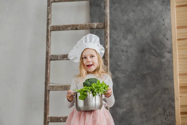 Niña hermosa sosteniendo una olla llena de verduras. Comida saludable. Cosecha. Pequeña ama de casa — Foto de Stock