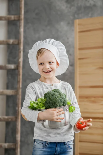 Hermoso chico guapo sosteniendo una olla llena de verduras. Comida saludable. Cosecha. Pequeño chef — Foto de Stock