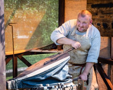 Ortaçağ elbisesi giyen yetişkin bir erkek demirci açık hava nalbantında çalışıyor. Orta Çağ Yaşayan Tarih Festivali 'nde demircilik yüksek lisansı.