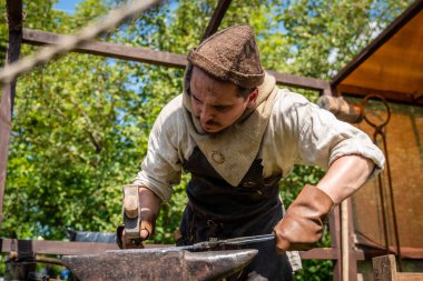 Ortaçağ giysileri içinde usta demirci açık hava ocağında çalışıyor. Orta Çağ Yaşayan Tarih Festivali 'nde demircilik yüksek lisansı.