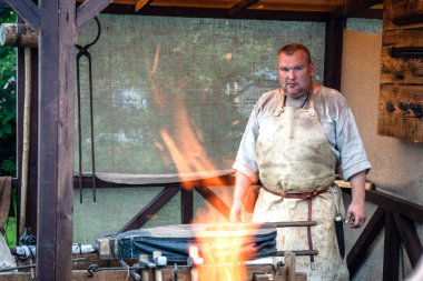 Açık ateşin yanında poz veren büyük erkek demirci. Yaşayan Tarih Festivali 'nde Ortaçağ Demircilik Atölyesi