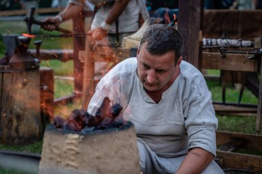 Bir nalbant, eski bir demircide çalışıyor. Yakın çekimde, arka planda Yaşayan Tarih Festivali 'nde Ortaçağ Demircilik Atölyesi var.