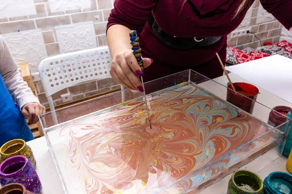 A master class in the art of Ebru, water painting, the ancient Turkish art of making paintings by applying pigments to the surface of a liquid. Close-up - the hand of a woman teacher puts a drawing on the surface of the water with a special tool