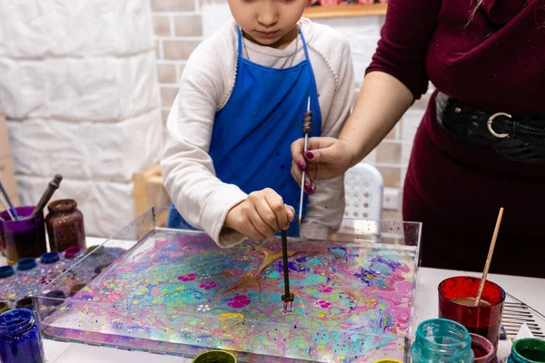 A master class in the art of Ebru, water painting, the ancient Turkish art of making paintings by applying pigments to the surface of a liquid. Close-up - children\'s and women\'s hands apply a drawing to the water surface with a special tool
