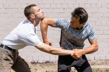 Dövüş sanatları eğitmenleri Krav Maga sokak dövüşlerinde kendini savunma tekniklerini gösterirler. - Evet. Defans, saldırganın elini engelliyor ve dirseğiyle karşı atağa geçiyor.