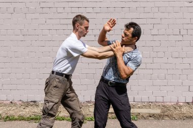 Dövüş sanatları eğitmenleri Krav Maga sokak dövüşlerinde kendini savunma tekniklerini gösterirler. Boğulmadan kurtulma tekniği, çatışmanın başlangıcı.