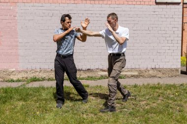 Dövüş sanatları eğitmenleri Krav Maga sokak dövüşlerinde kendini savunma tekniklerini gösterirler. Savunma, saldırganın elini engelliyor. 