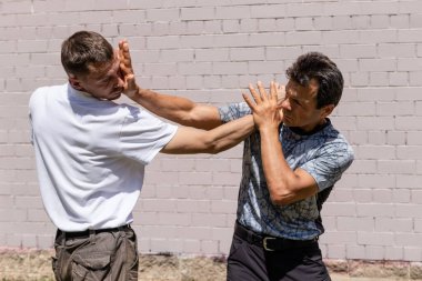 Dövüş sanatları eğitmenleri Krav Maga sokak dövüşlerinde kendini savunma tekniklerini gösterirler. Savunma, saldırganın elini engeller ve saldırganın yüzüne vurur.