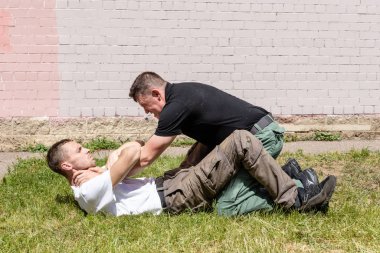 Martial arts instructors Krav Maga demonstrate self-defense techniques in a street fight. Release from capture in a prone position. Defender fixes the opponents hands . clipart