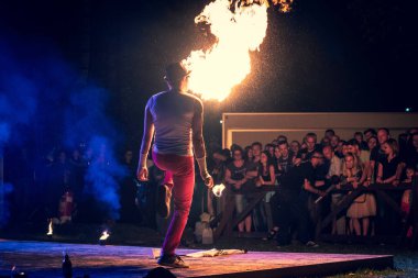 Erkek sanatçı izleyicilere ateş püskürüyor, yaz açık hava festivalinde yangın gösterisi gösterisi gösterisi