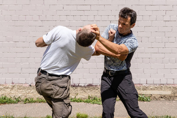 Martial arts instructors Krav Maga demonstrate self-defense techniques in a street fight. Defender blocks the attacker's hand and applies brutal technique with his face. 