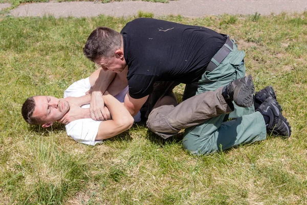 The man fixes the opponents hands in a fight in the supine position and prepares to free himself from the grip. Martial arts instructors Krav Maga demonstrate self-defense techniques in a street fight