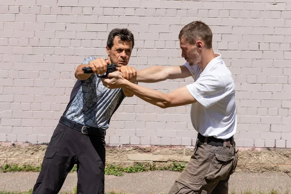 Dövüş sanatları eğitmenleri Krav Maga sokak dövüşlerinde kendini savunma tekniklerini gösterirler. Savunma, silahı eliyle blokluyor ve atışı engelliyor..