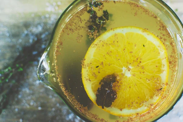 Sarı aromatik meyve çayı, bir dilim limon ve lezzet ve biberiye, cam bir kasede, üst manzara. Ahşap bir arka planda kompozisyon için yeşil bir biberiye filizi uzanır.