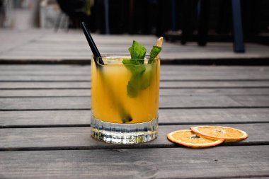 Kuru portakalla süslenmiş buzlu portakal kokteyli ve taze yeşil nane filizi. Düz yatay tahtaları olan ahşap bir zemin üzerinde kompozisyon