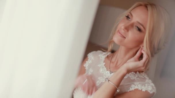 Pretty bride looking out of window and smiling on her wedding day — Stock Video