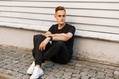 Şık siyah giysiler ve ahşap bir duvarın yanında dinlenmiş beyaz ayakkabı güzel hipster adam