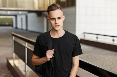 Modern bir binanın arka planda duran bir sırt çantası ile siyah gömlek yakışıklı genç adam.