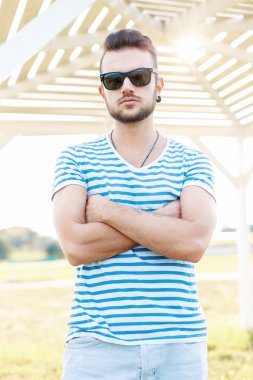 Güneşli bir günde sahilde duran bir yaz gömlek ve güneş gözlüğü sakallı yakışıklı adam.
