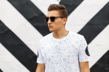 Güneş gözlüğü ve bir arka plan siyah ve beyaz çizgiler noktalar olan beyaz bir tişört yakışıklı adam.