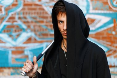 Bir tuğla duvar grafiti ile yakınındaki bir başlık konumu olan siyah giysili şık yakışıklı adam. Adam holding yarasa.