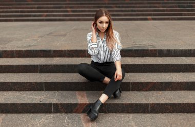 Çizgili bir bluz, siyah kot pantolon ve ayakkabı merdivenlerde oturan güzel kadın
