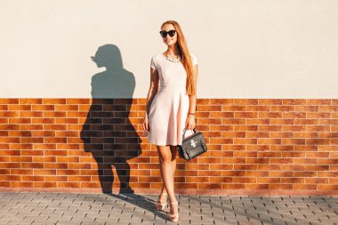 Tuğla duvar yakınındaki ihale güneş gözlüğü, pembe elbiseli şık güzel kadın