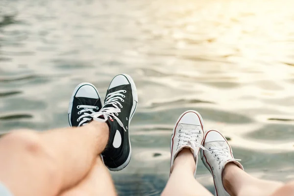 Een jong stel op het strand. Benen met sneakers bij het water — Stockfoto