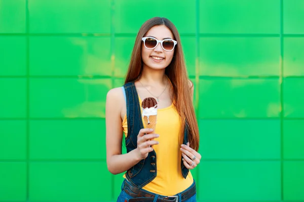 Веселая красивая молодая женщина улыбается, держа мороженое возле ярко-зеленой стены — стоковое фото