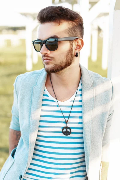 Bel homme en lunettes de soleil dans une veste élégante et des lunettes de soleil sur le fond de la plage — Photo