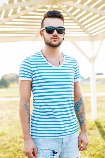 Trendiger gutaussehender Hipster mit Bart und Sonnenbrille im trendigen Hemd steht am Strand. — Stockfoto