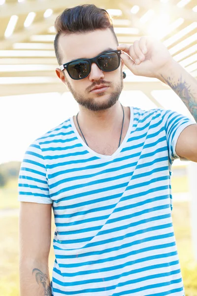 Schöner Mann im stylischen Sommerhemd korrigiert Sonnenbrille am Strand. — Stockfoto