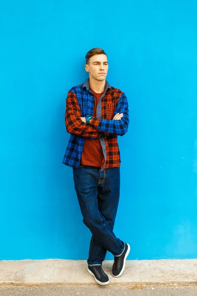 Jonge knappe man in stijlvolle kleding en sneakers poseert bij de blauwe muur — Stockfoto