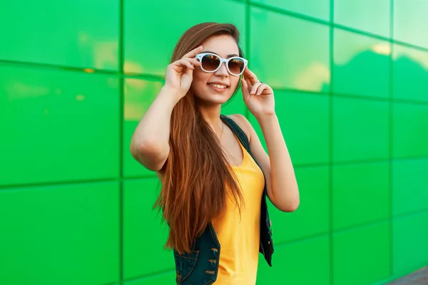 Feliz mujer alegre y elegante en gafas de sol posando cerca de la pared verde brillante . — Foto de Stock