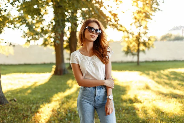 Schönes junges Mädchen in weißem T-Shirt und Vintage-Jeans mit Sonnenbrille an einem sonnigen Tag im Park. — Stockfoto