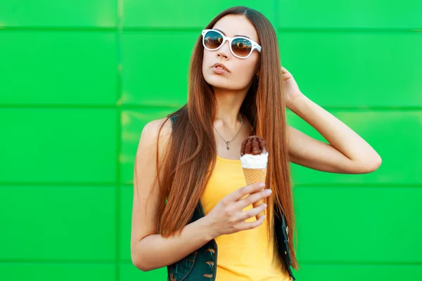 Красивая молодая женщина с мороженым в солнечных очках стоит у зеленой стены . — стоковое фото