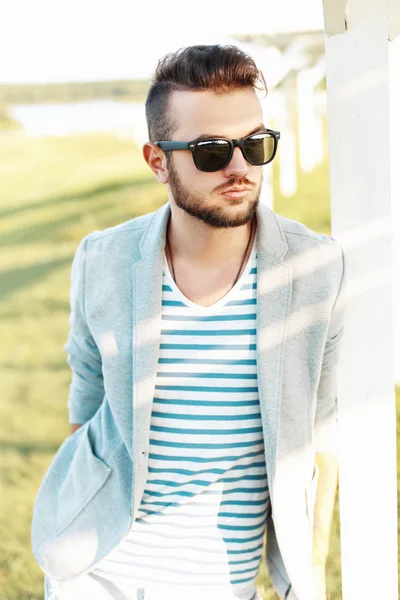 Schöner Hipster in Jacke, sommerlichem T-Shirt und Sonnenbrille an einem sonnigen Tag. — Stockfoto