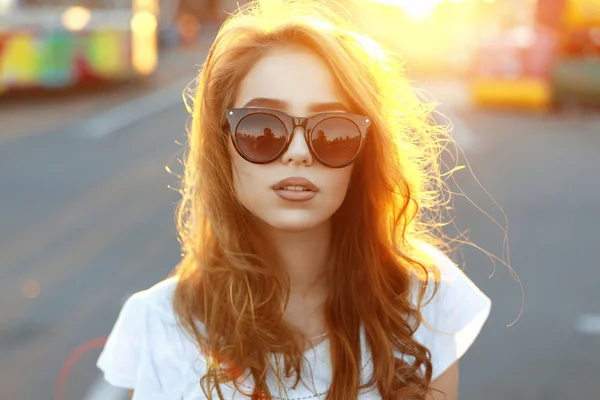 Belle jeune fille hipster dans des lunettes de soleil à la mode debout sur la plage sur le coucher de soleil incroyable — Photo